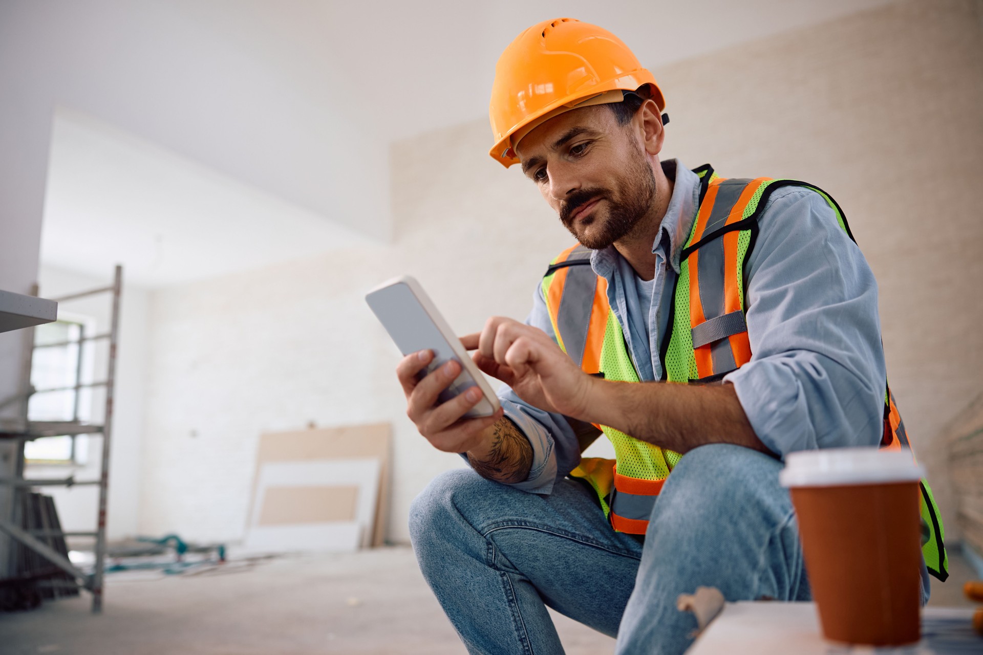 Smiling worker using smart phone at construction site.